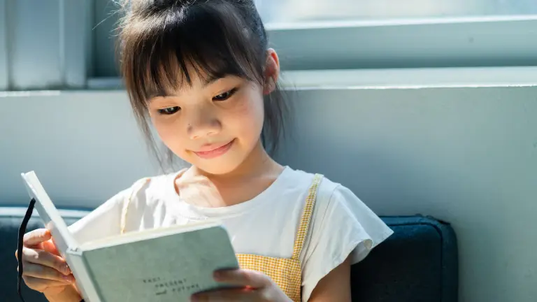 Child reading a book to improve 11+ reading comprehension skills.