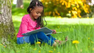 Child reading a book outdoors during the summer holidays to maintain reading skills.