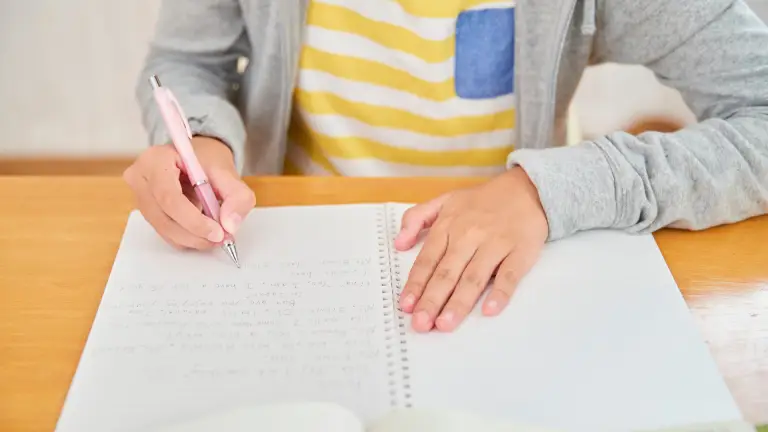 Child writing in a notebook to practise writing skills during the summer break.
