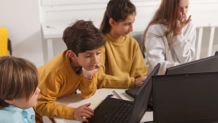 Secondary school students learning together in a small group using laptops.