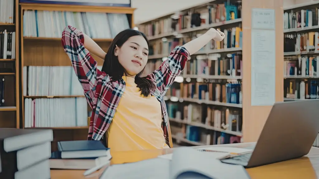 Teenage student relaxing on a sofa and reading a book during a study break.